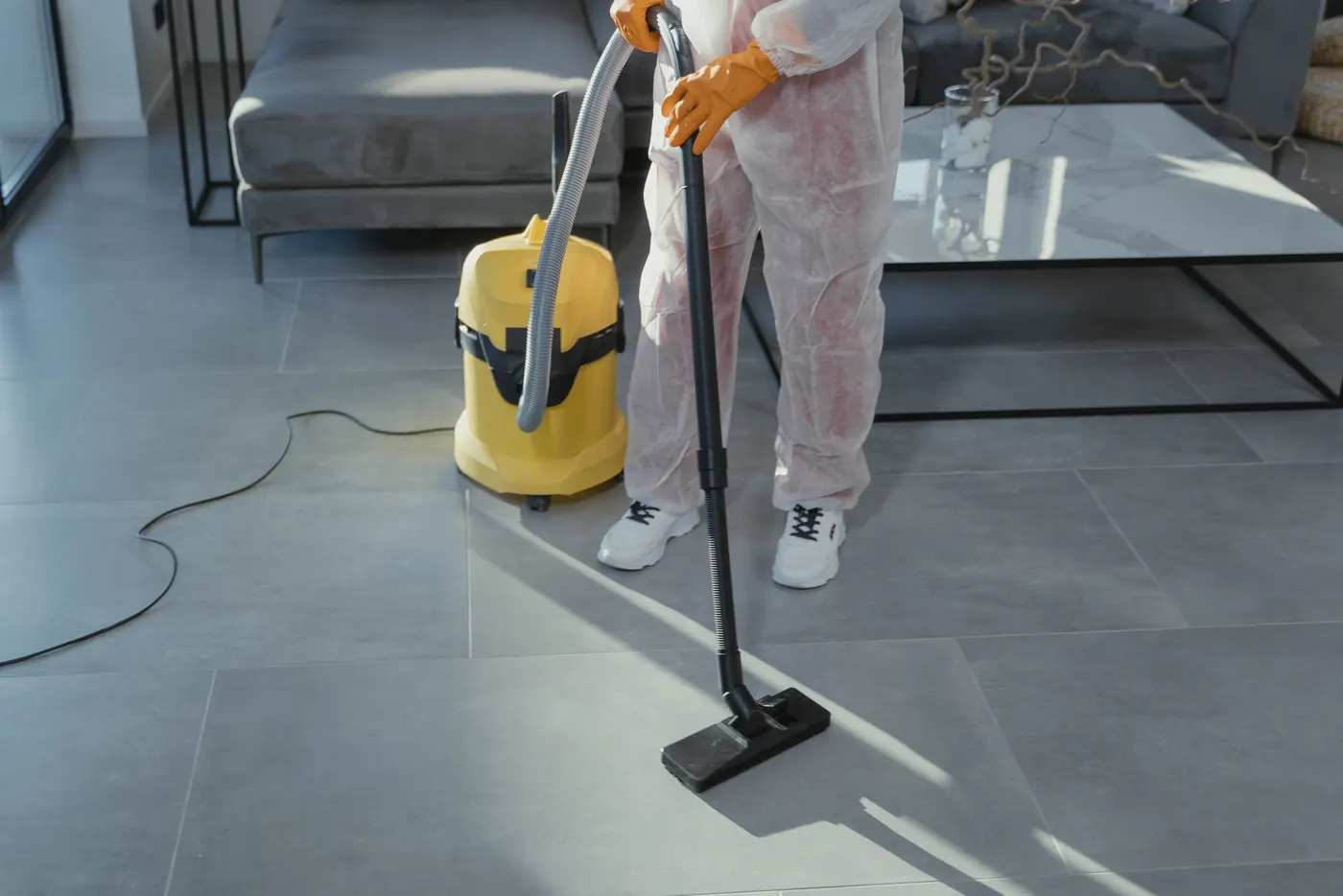Cleaner in protective coveralls vacuuming a hard floor with a commercial machine