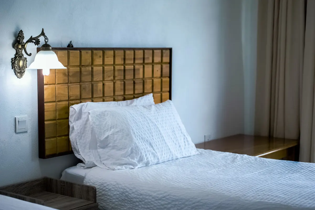Bedroom with a tufted brass panel headboard, crisp white bedding and a wall-mounted reading lamp