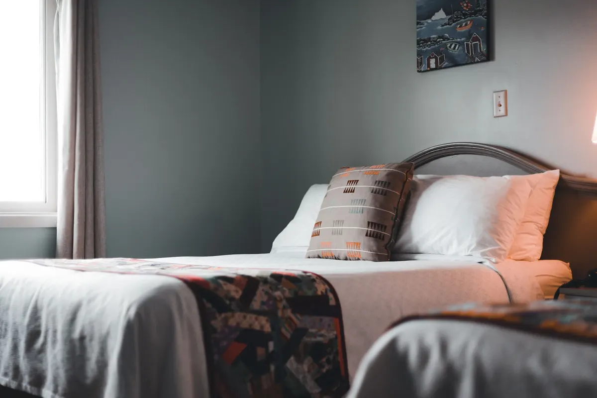 Bedroom with soft gray walls, a made bed with a patterned throw, framed art and a curtained window