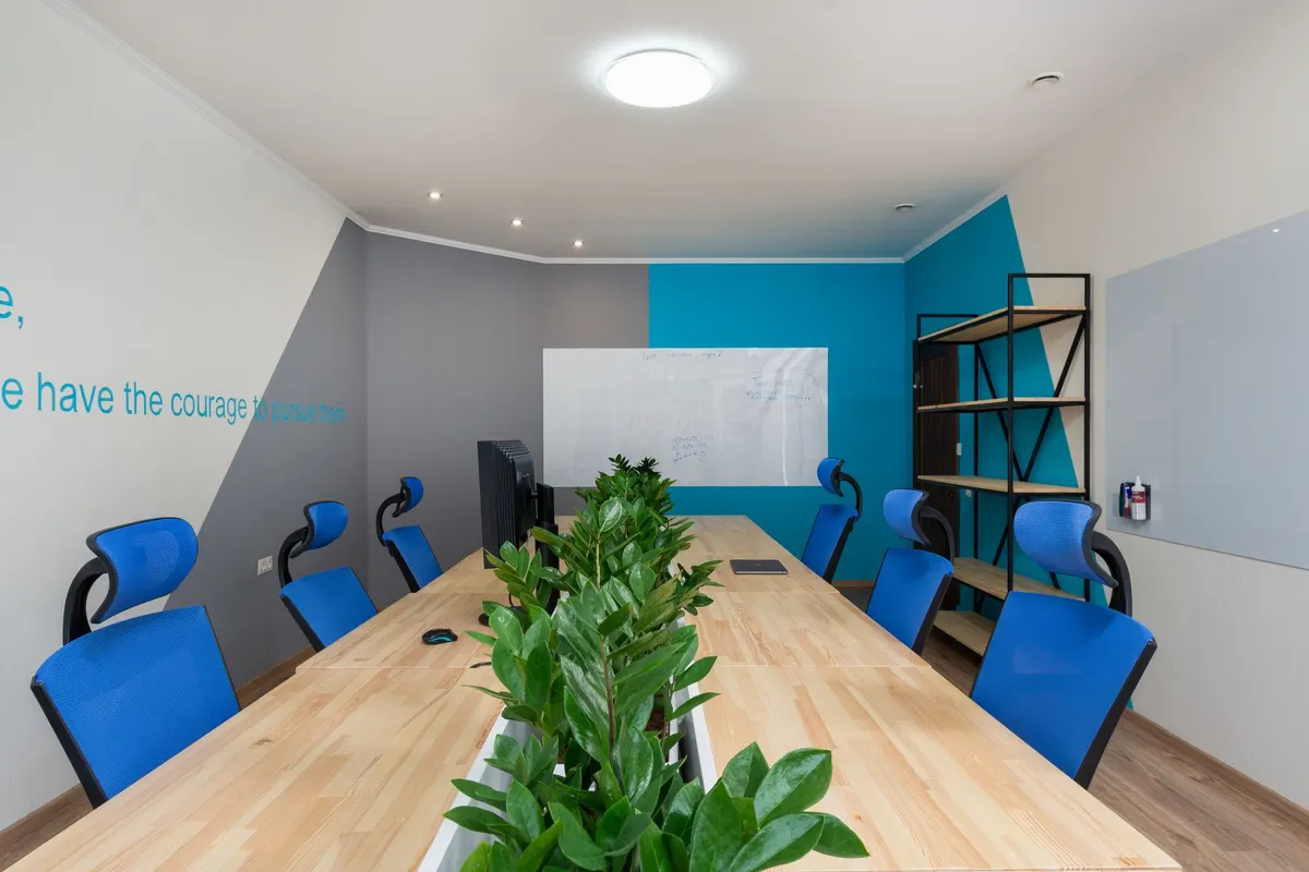 Conference room with a long wooden table, blue chairs, a potted plant and a wall-mounted whiteboard