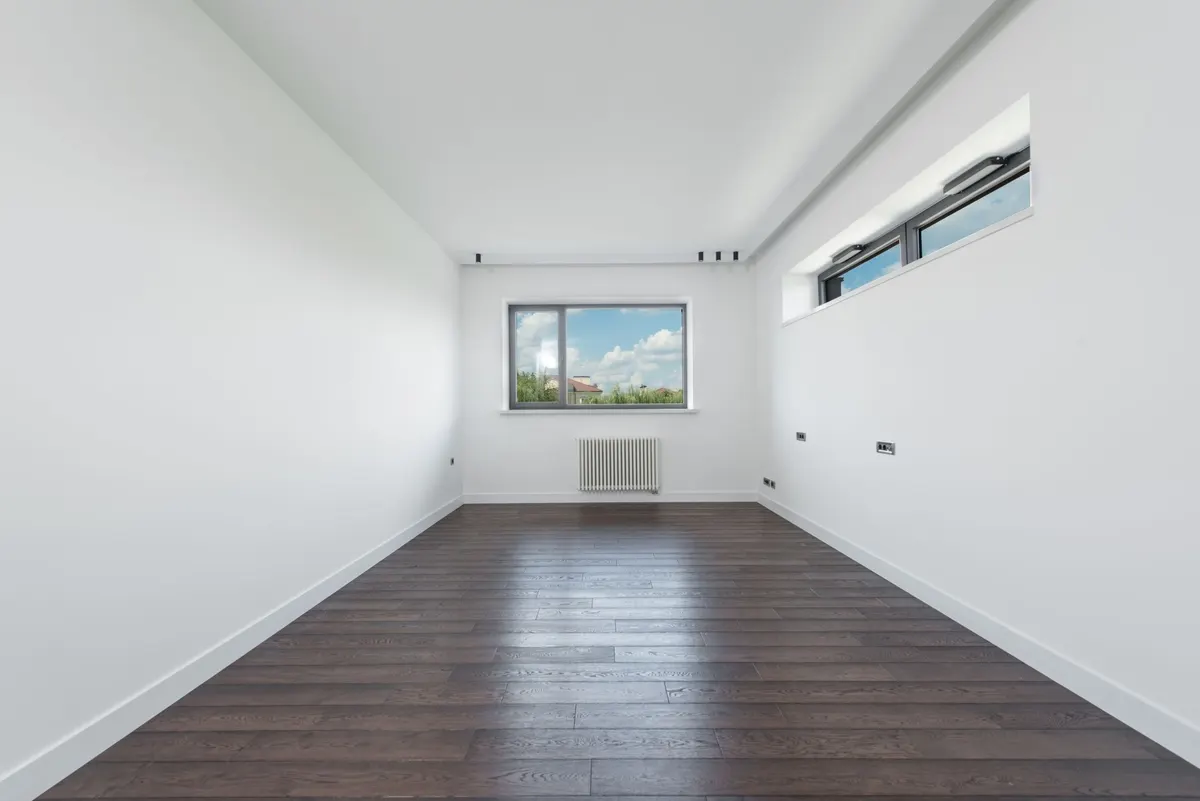 Empty room with white walls, dark wood flooring and a high window, cleared ready for handover