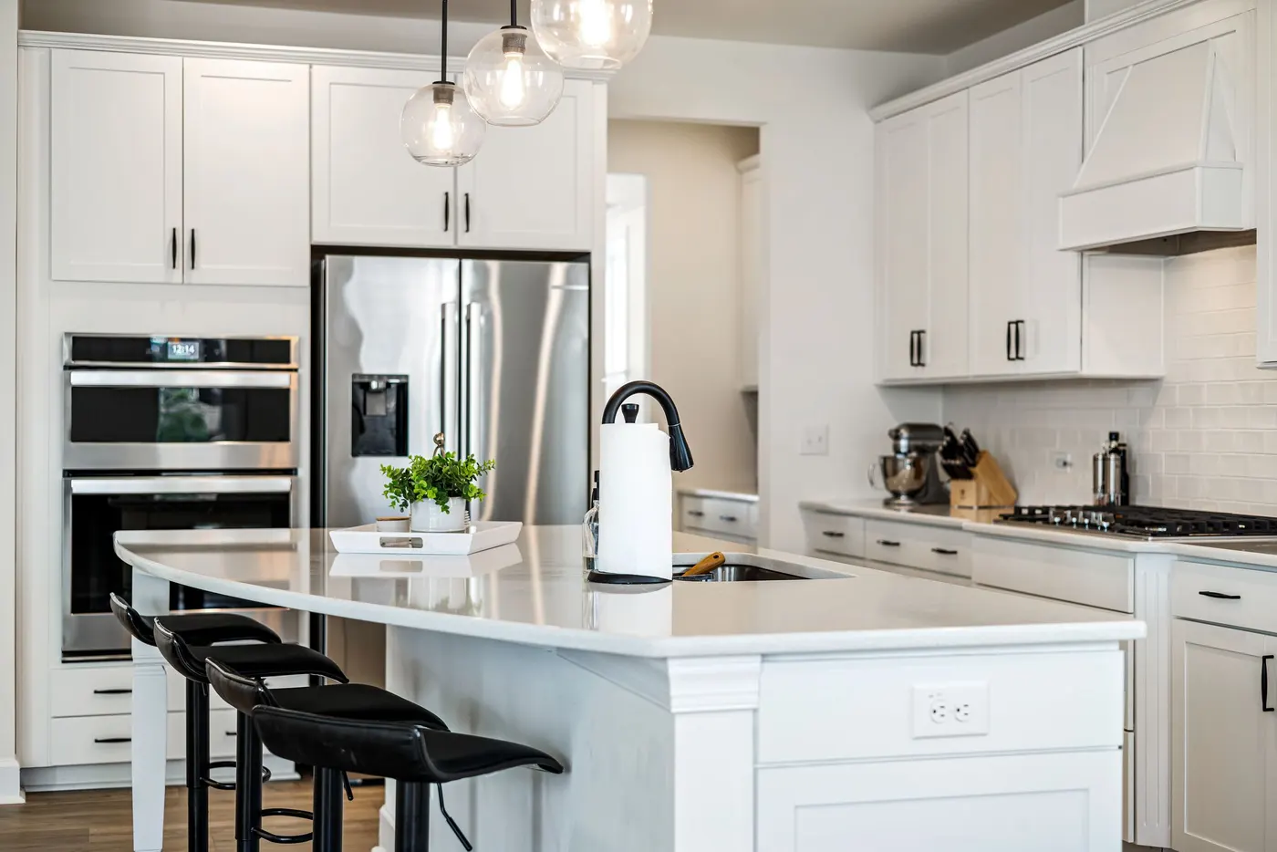 Bright white kitchen with a large center island, pendant lights, stainless steel refrigerator and built-in double wall ovens