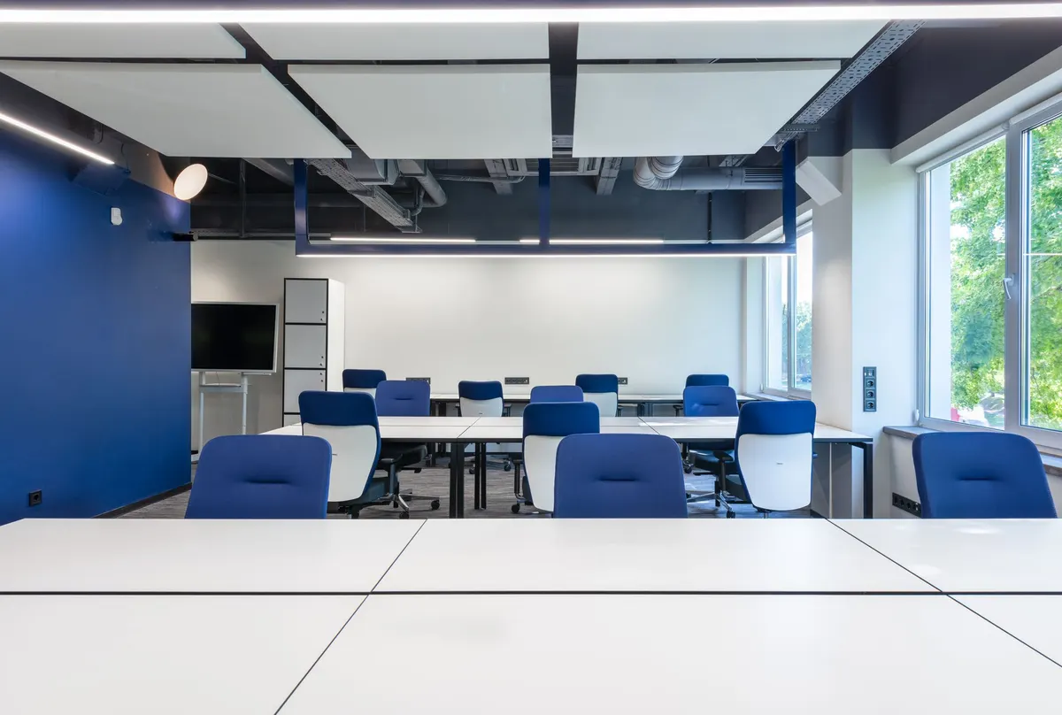 Open office with rows of white desks, blue task chairs and a window wall along one side