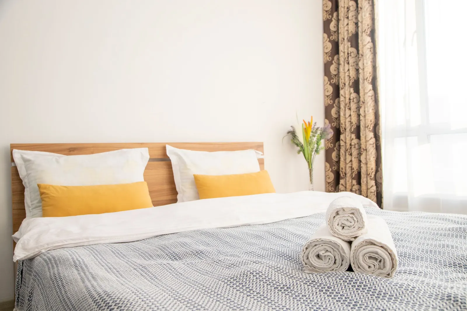 Guest bedroom made up with fresh white linens, yellow accent pillows and rolled towels on the bed