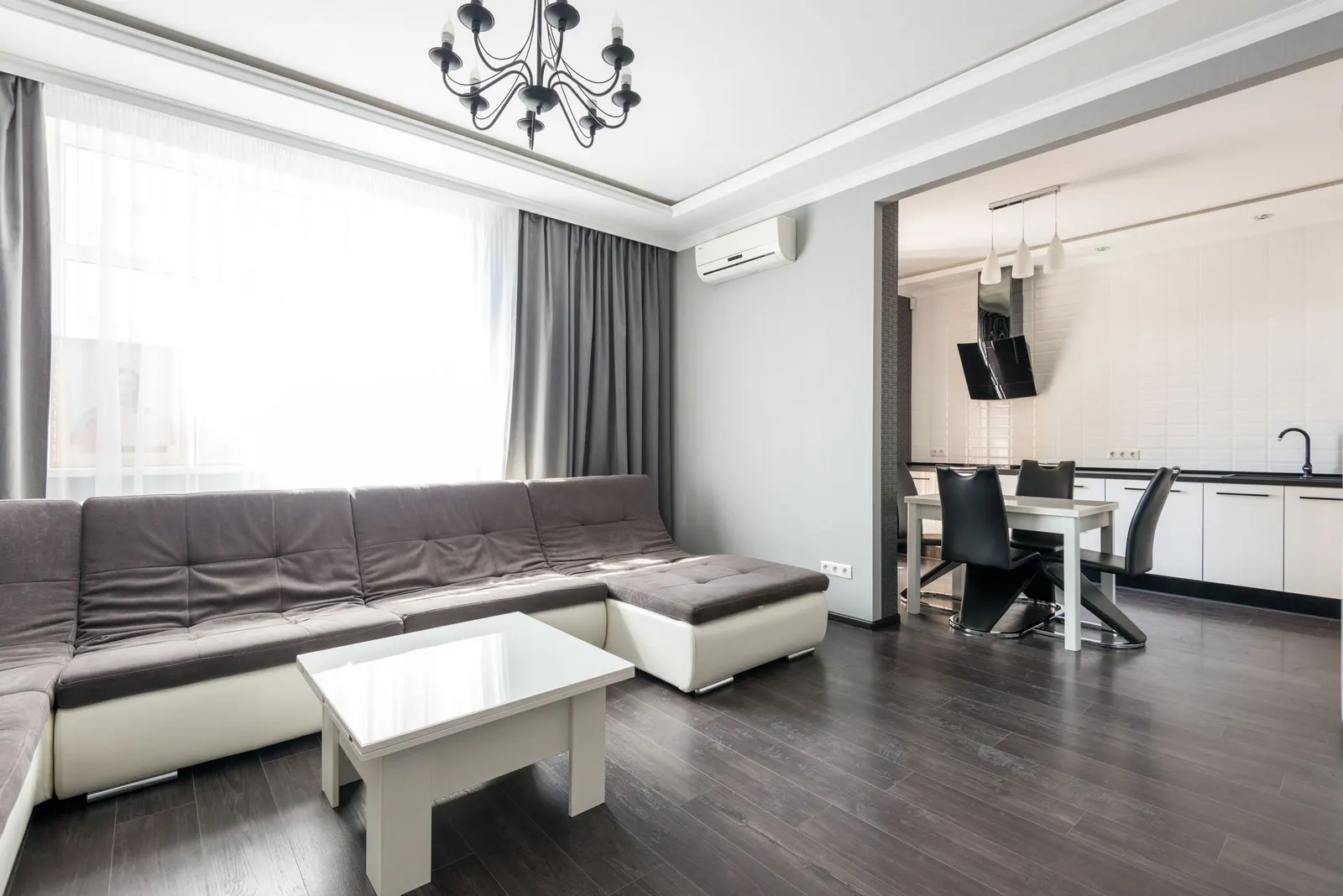 Modern apartment interior with a gray sectional sofa, glass coffee table and a dining and work zone by the window