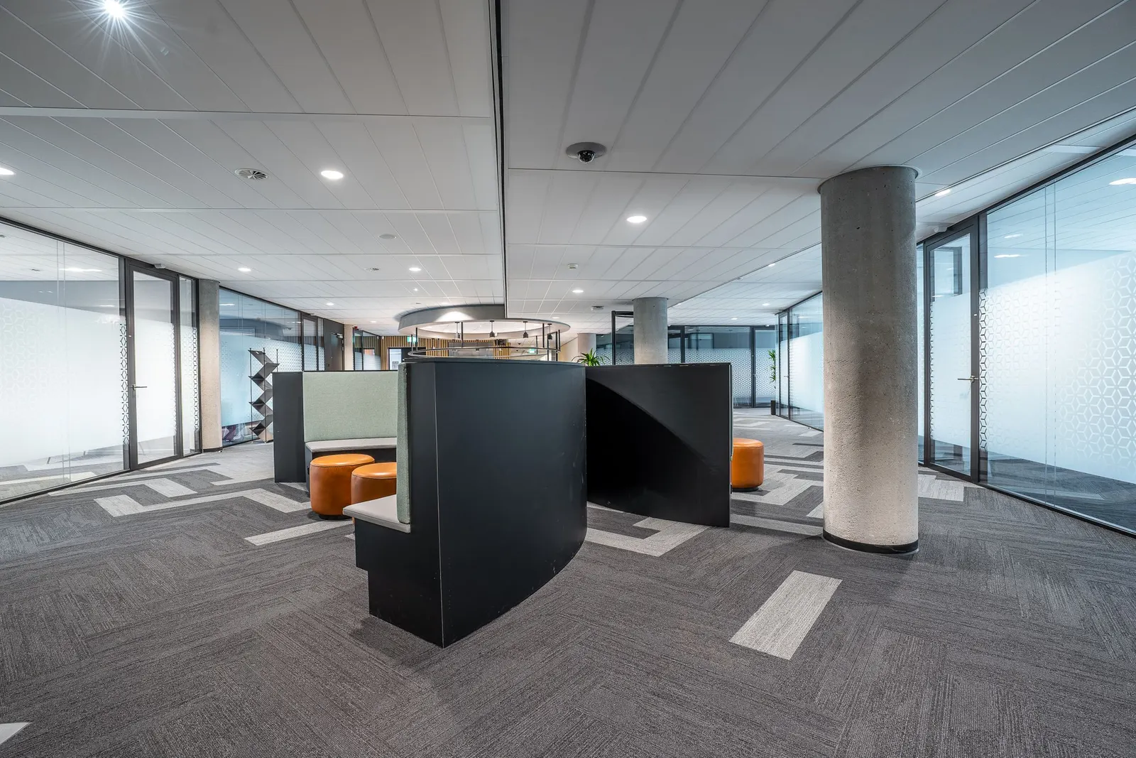 Open commercial office floor with workstations, structural columns and daylight from a window wall