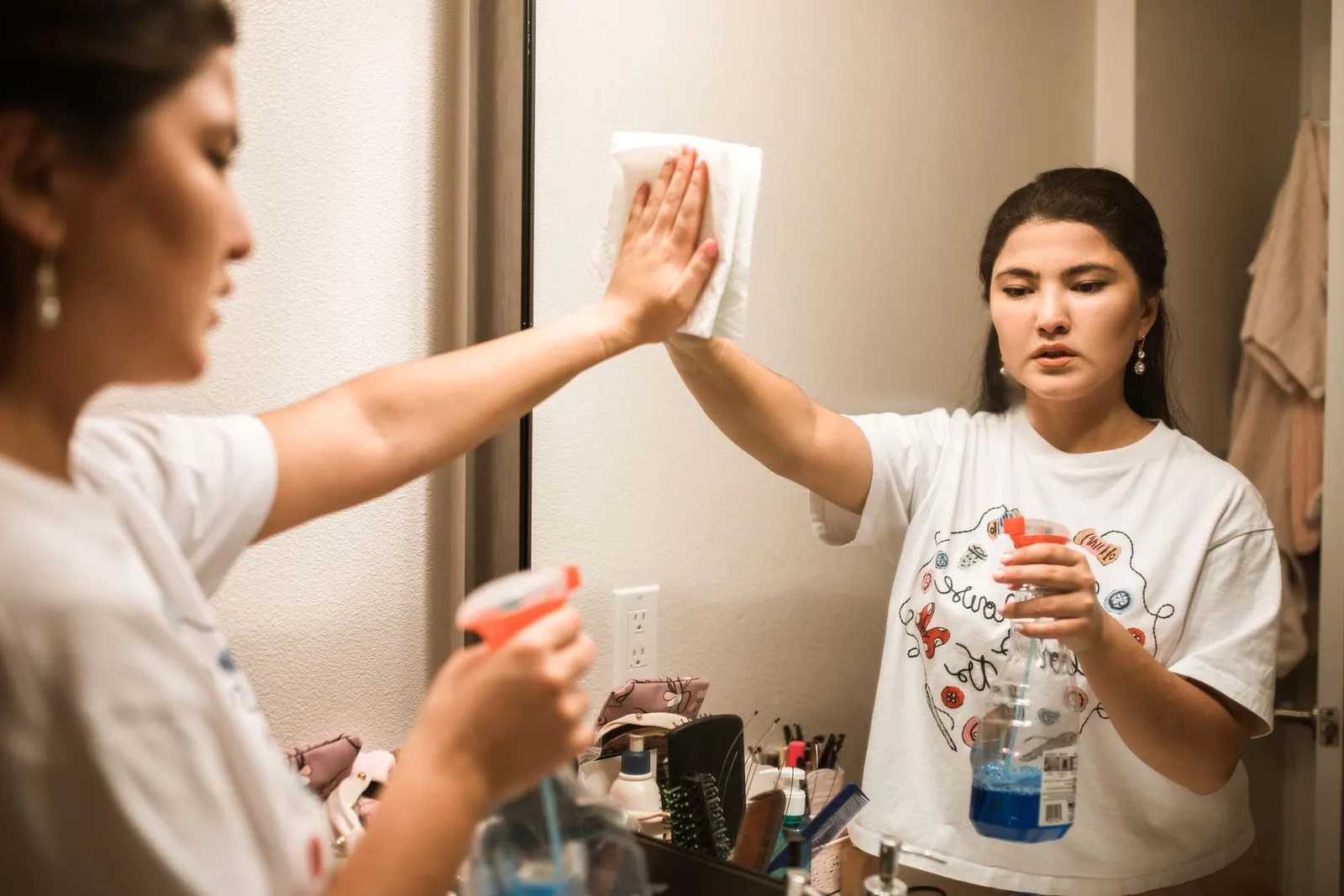 Cleaner in a home spraying and wiping a wall mirror with a microfiber cloth