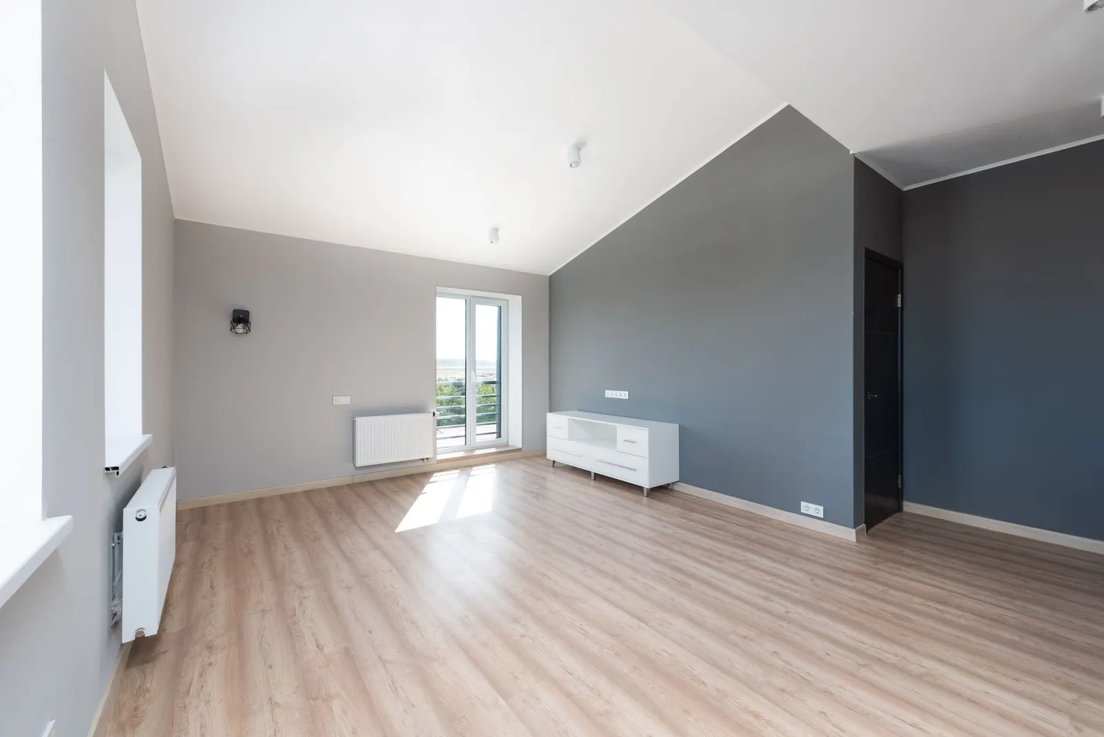 Empty apartment room with bare hardwood floors, white walls and a bright window