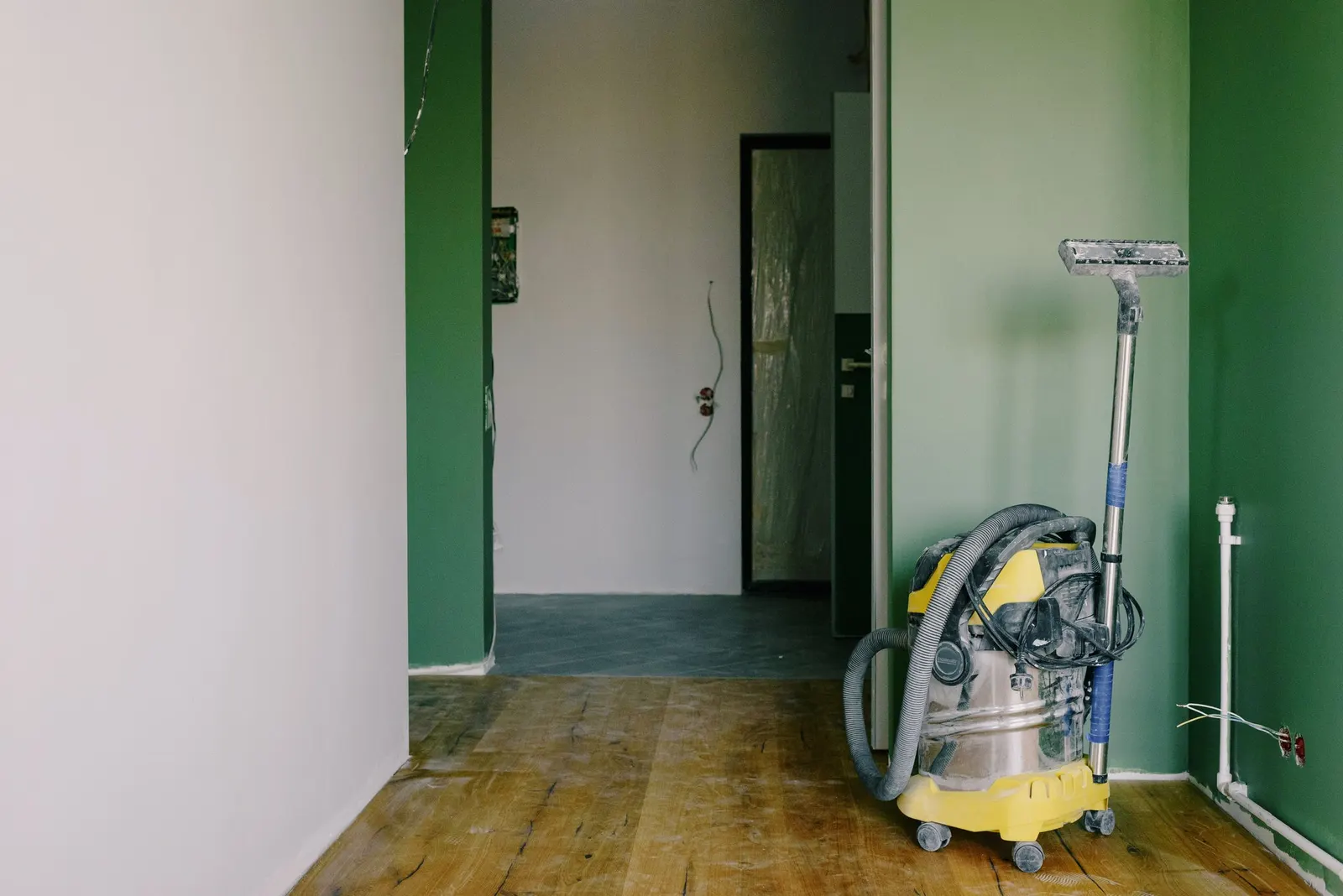 Bare room mid-renovation with an industrial vacuum on a wood floor and freshly painted walls