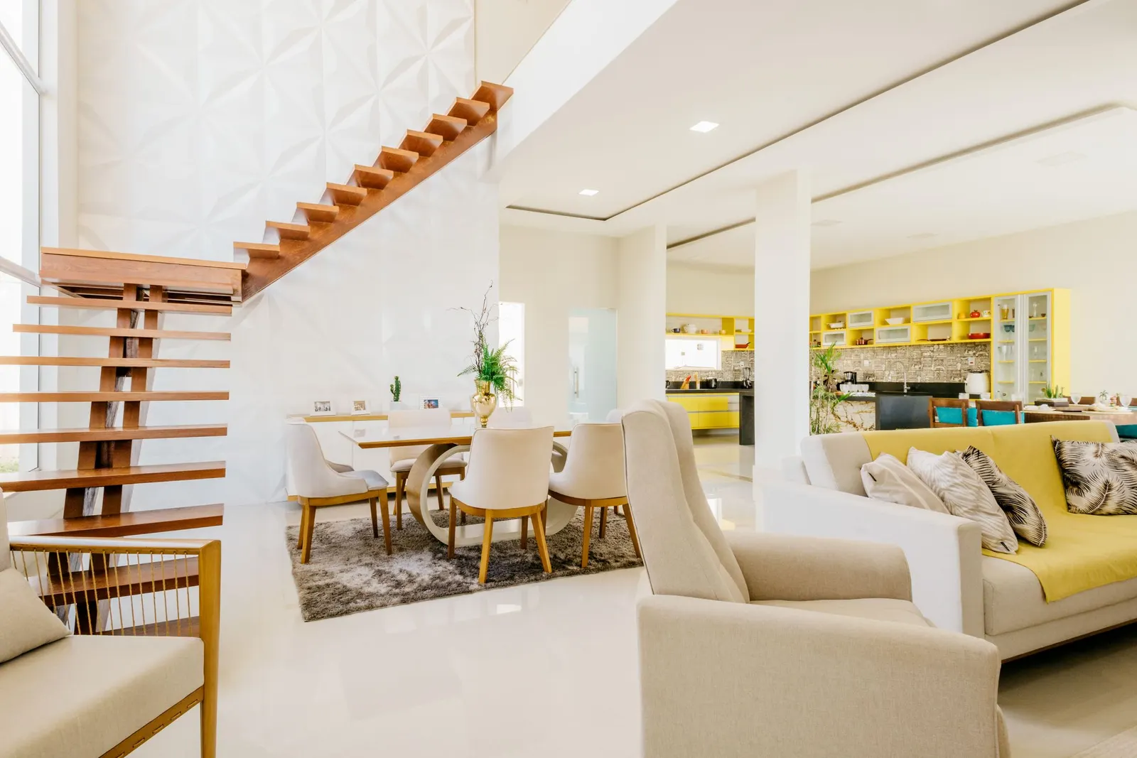 Open-plan living and dining area kept tidy, with a staircase, armchairs and daylight from tall windows