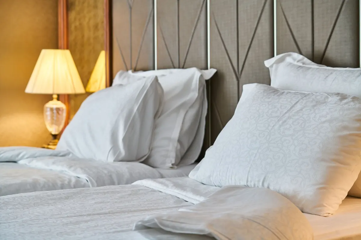 Freshly made bed with crisp white pillows and linens beside a lit bedside lamp